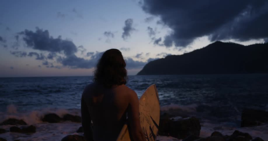 Surfer stands on a beach at sunset