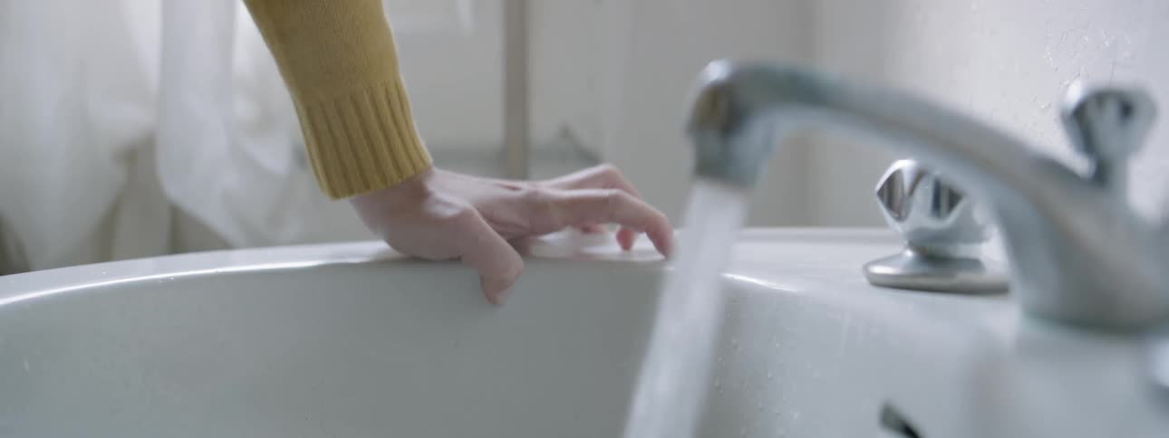 A woman turns on a bathroom faucet