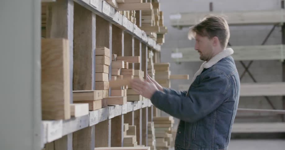A man is selecting and removing a wood board from a shelf in a warehouse