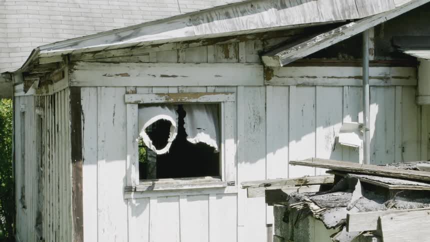 Curtains are blowing in the open window of a shack during the day