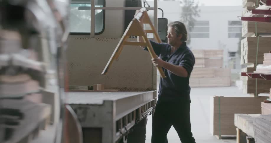 A man is carrying a part of a rack and placing it on a truck in a lumberyard