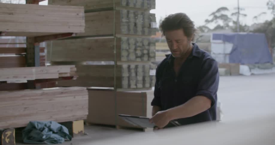 A man is checking his clipboard as he works in a lumberyard during the day