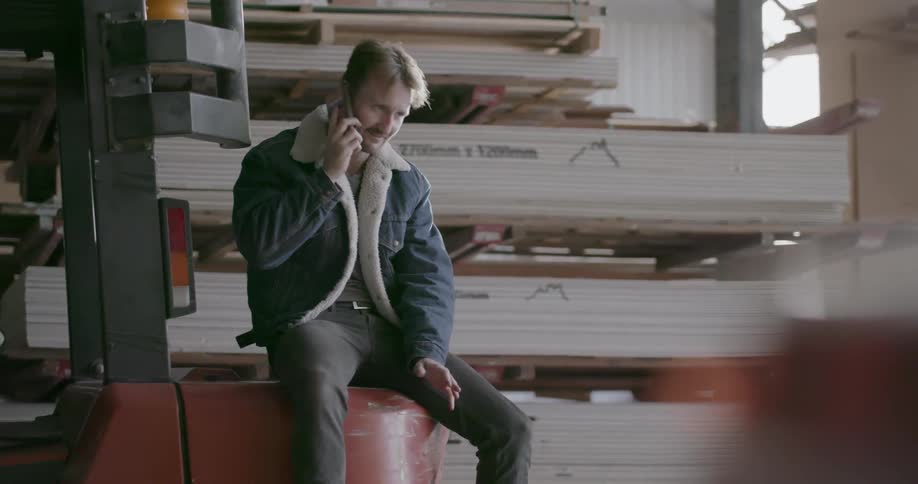 Man talks on a phone while sitting in a lumber warehouse
