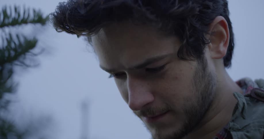 Man's face looks down while standing next to a pine tree