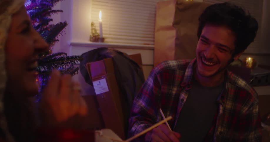 A man and woman eat chinese food by the christmas tree