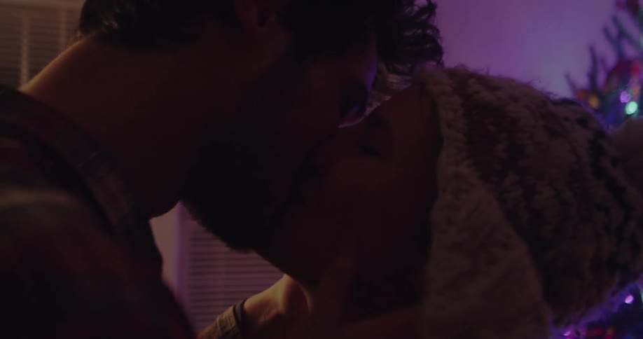 A man and woman kiss and embrace in front of a christmas tree