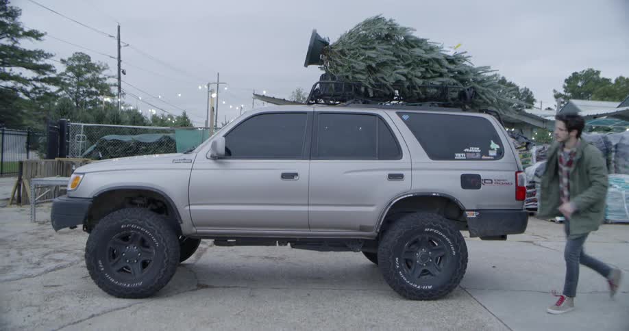 A man secures a christmas tree on the roof rack then gets in the suv