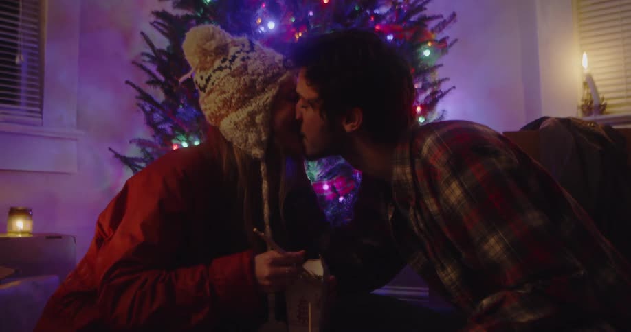 A man and woman share a kiss and chinese food in front of a christmas tree