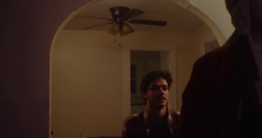 A man covers a woman's eyes playfully as they walk through a house