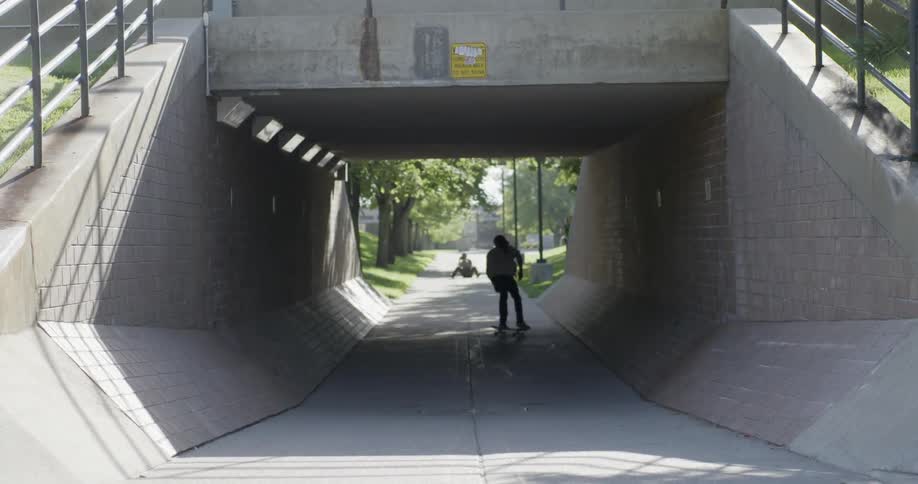 Man riding a skateboard into a overpass tunnel