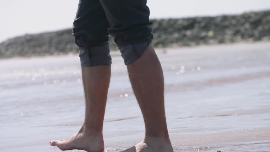 A man is walking barefoot into the tide on a beach during the day