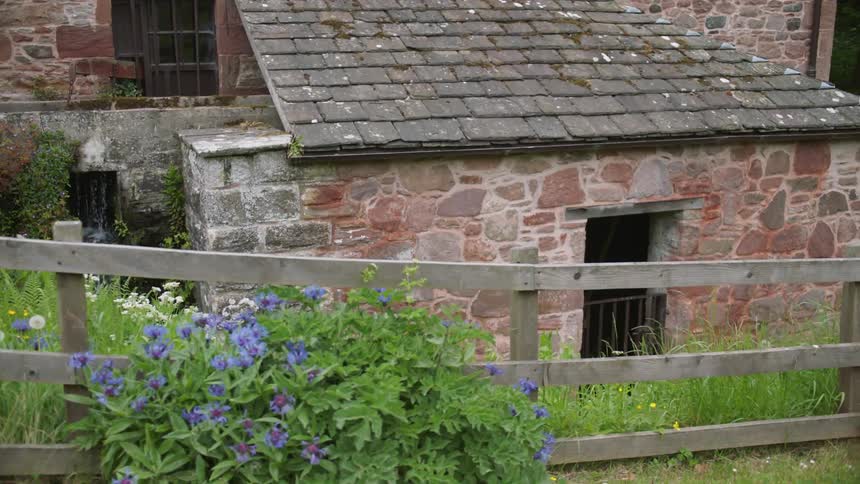 Wooden fence borders the lawn of a stone farmhouse