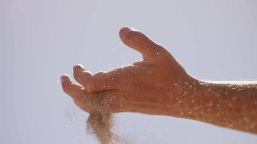 Small particles flowing form a fist as it releases them on a clear day