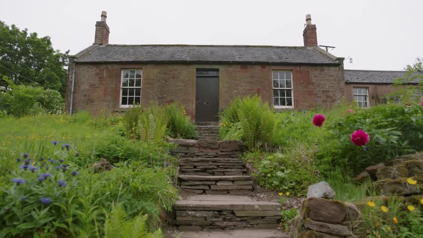 Grass and flowers line the walkway leading to the brick house