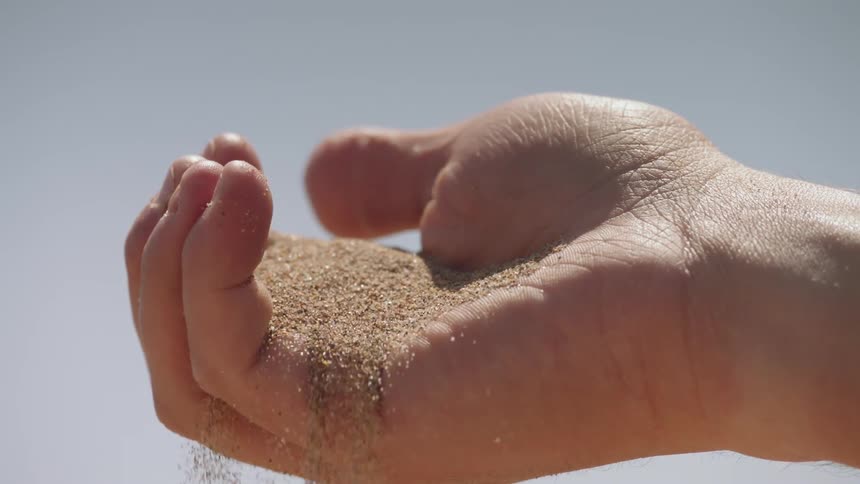 Sand sifts and falls from a person's hand on a sunny day