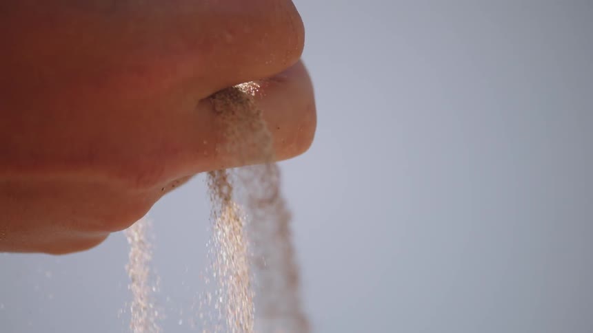 Sand falls through a person's fingers