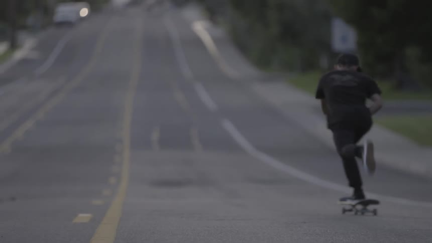 Man rides a skateboard down the street and does a kick flip