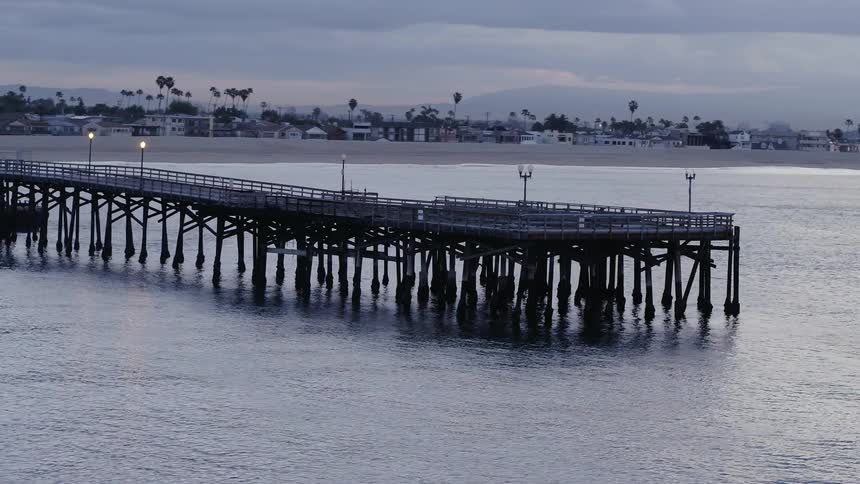 The ocean tide is rolling beneath a pier on the coast at dusk
