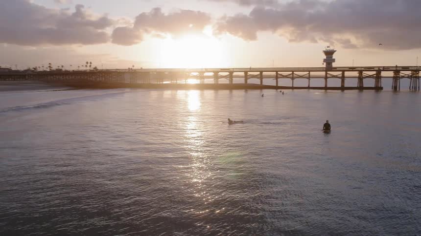 Surfers are paddling and floating in the ocean at dusk