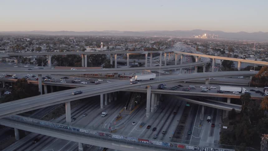 Cars drive on a city highway system at sunrise