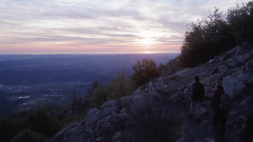 People hiking up a rocky hill at sunrise