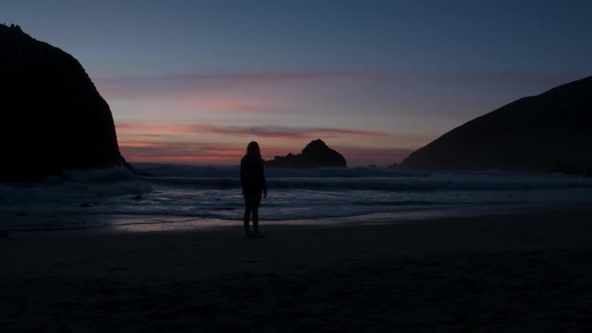 Person stands outside at sunset looking out at the water