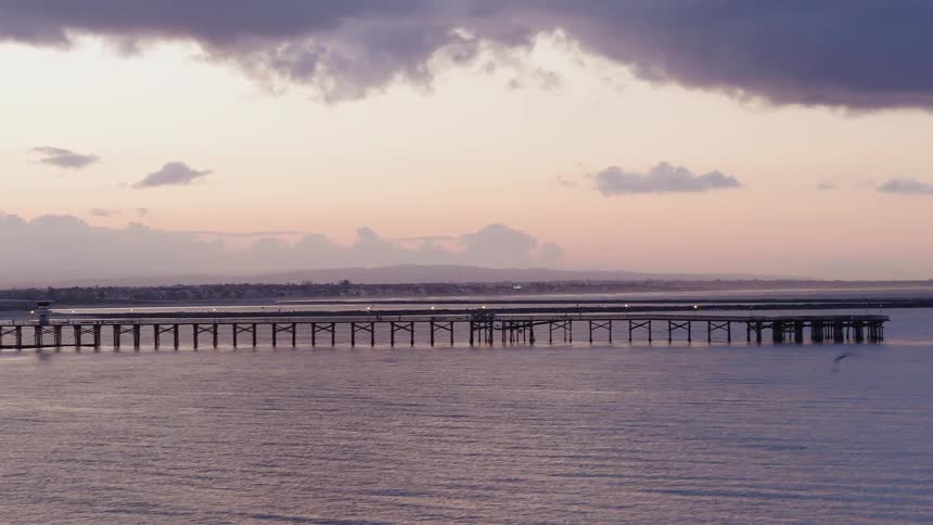 Waves are rolling onto a beach near a pier at dusk