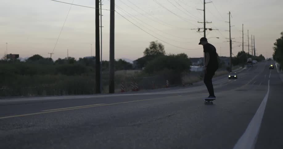A skateboarder kickflips his board while riding down a street
