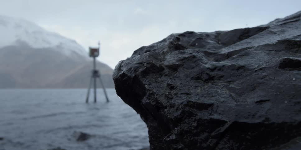Snow falls around a rock on a lakeshore
