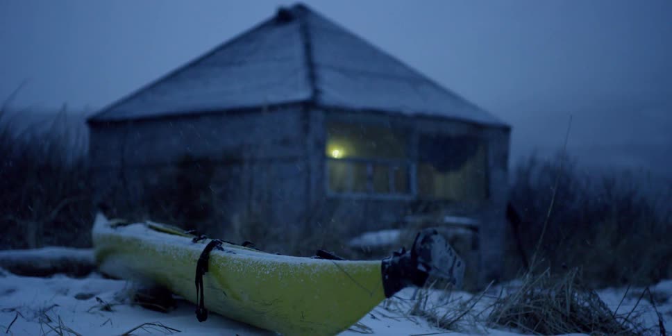Snow falls on a cabin and kayak