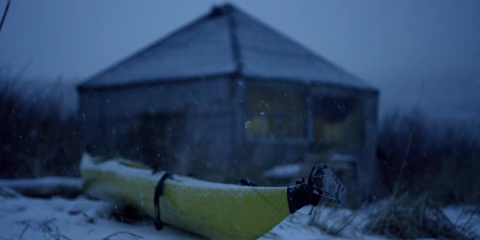 Snow falls on a cabin and kayak