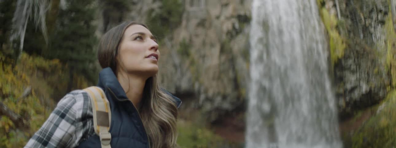 A woman stands near the waterfall looking around