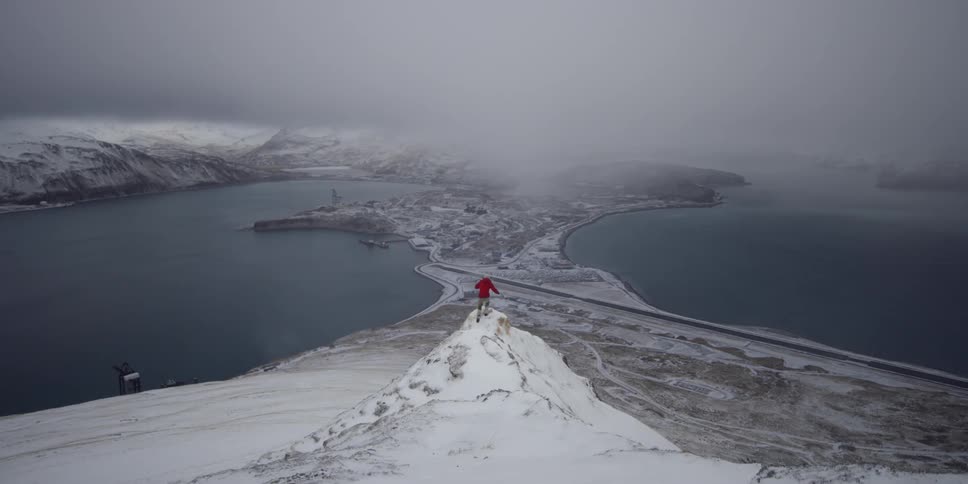 A person walks on a snowy ridge above town