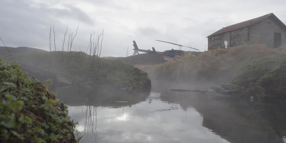 Mist is drifting across an inlet near a cabin during the day