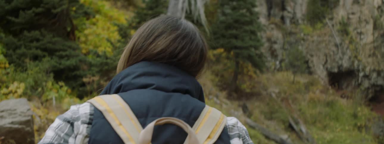 A woman with a backpack is hiking through the woods