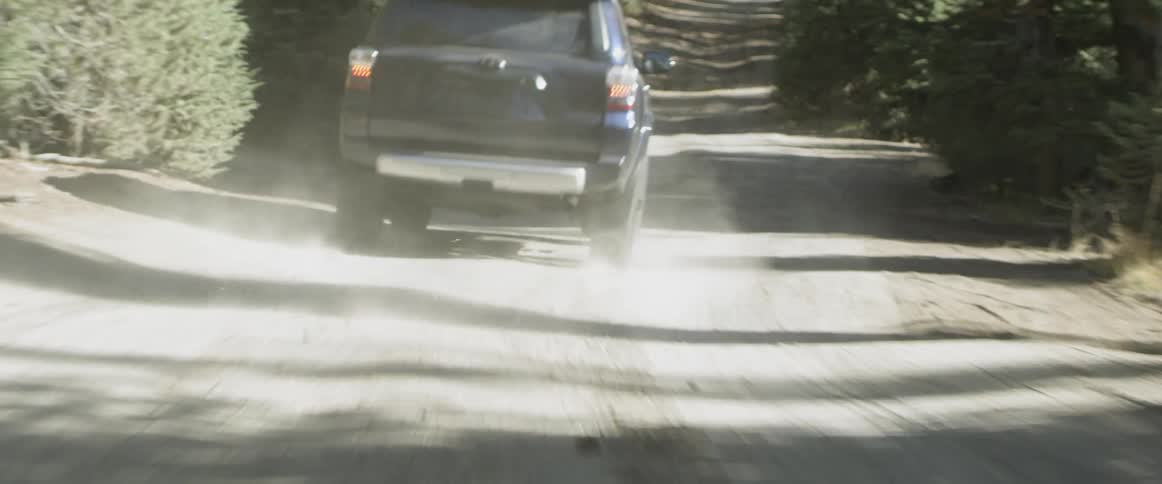 An suv is driving on a dirt road through a forest during the day