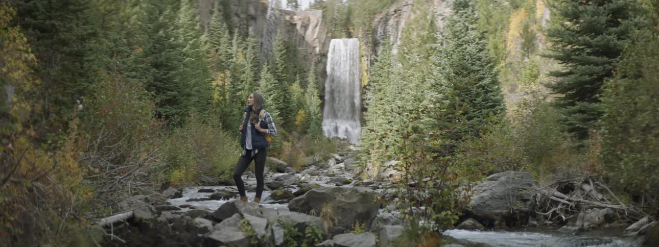 A hiker stands near a waterfall in the wilderness