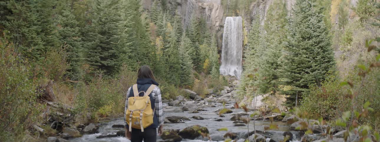 A woman walks towards the waterfall and stops