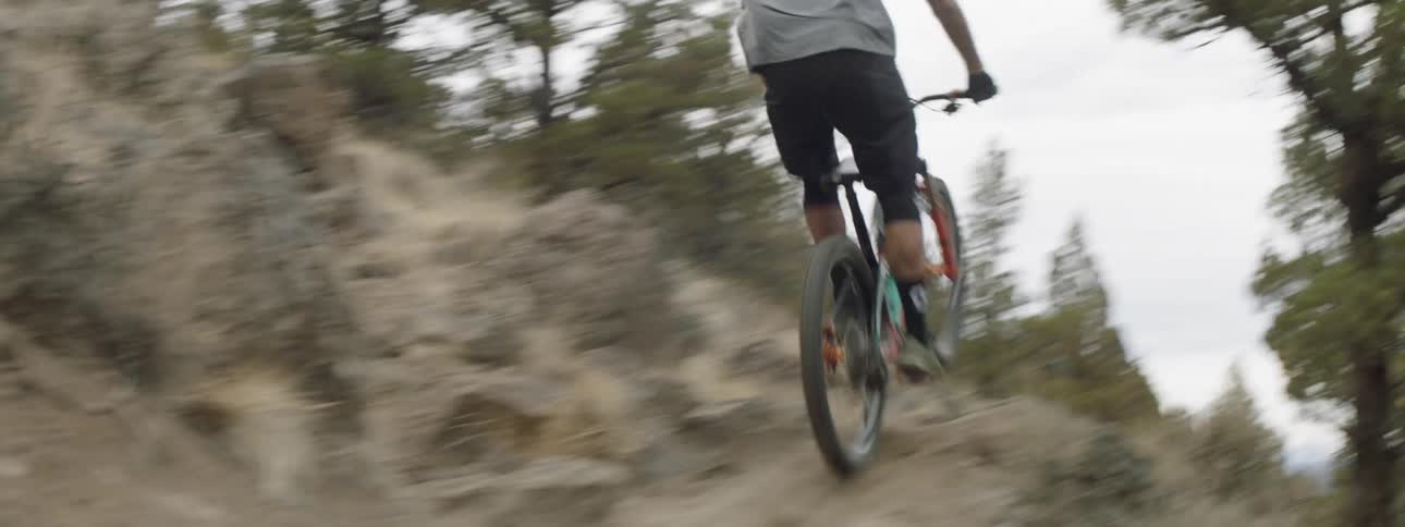 A guy is riding a mountain bike down a dirt trail and takes it over a jump