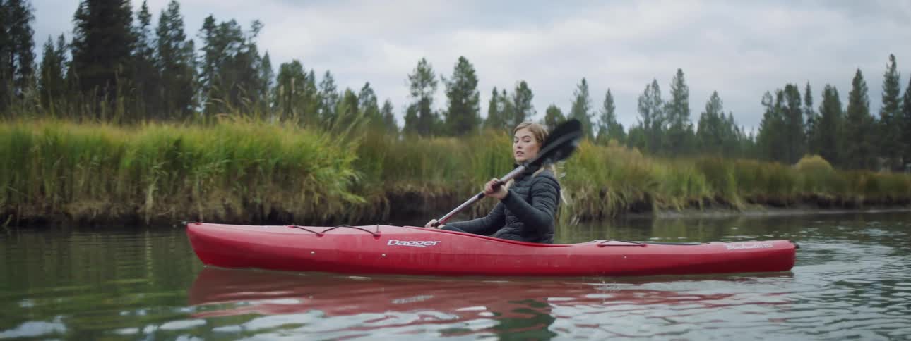 A woman is rowing a kayak in a river on a cloudy day