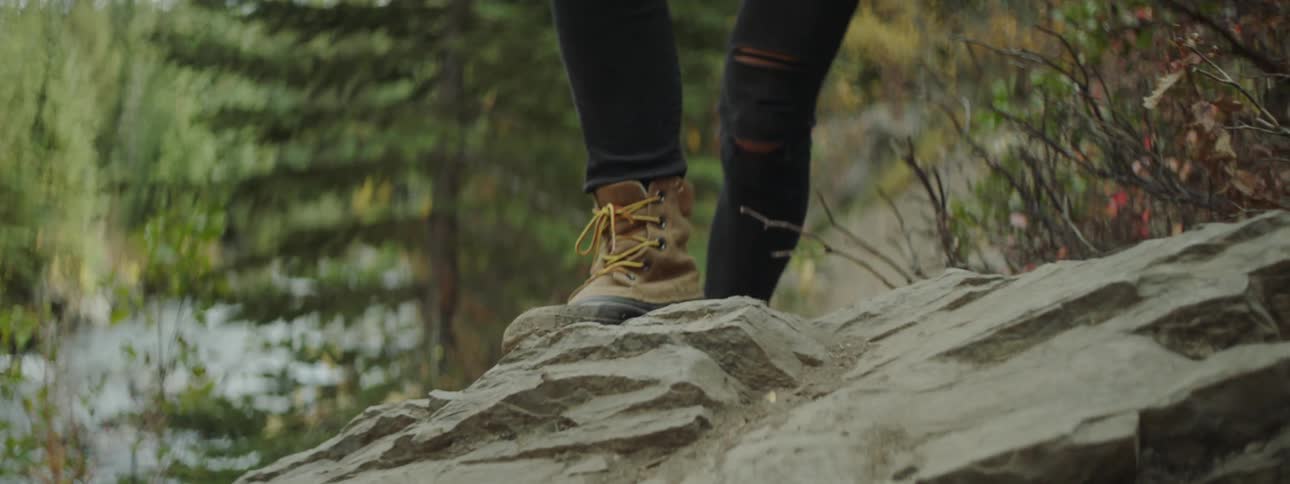 A woman hikes up a large rock in the woods