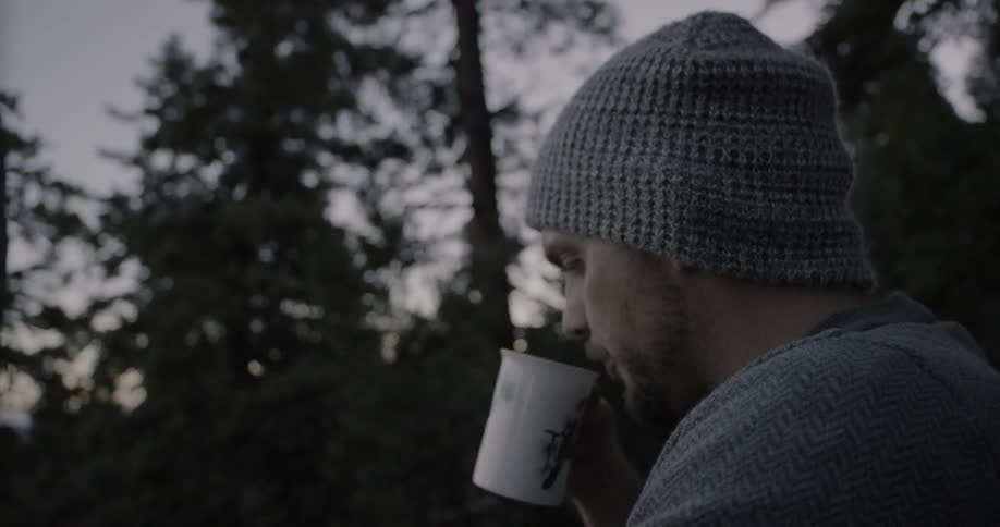 A man sips coffee in a forest at dusk