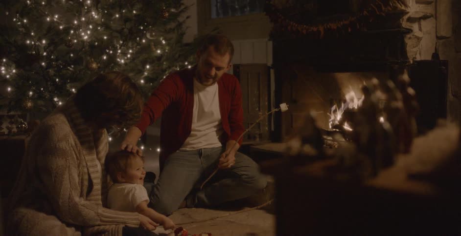 A family roasts marshmallows in a fireplace at christmas