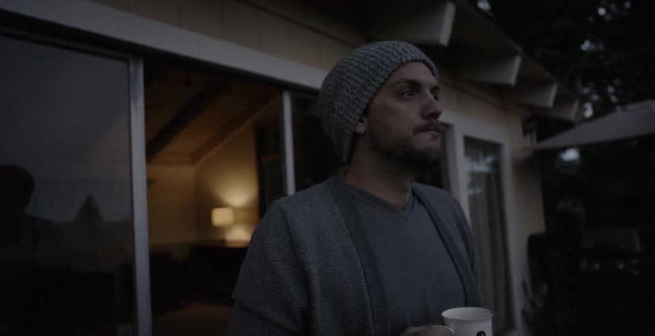 Man holds a mug and stands outside patio door