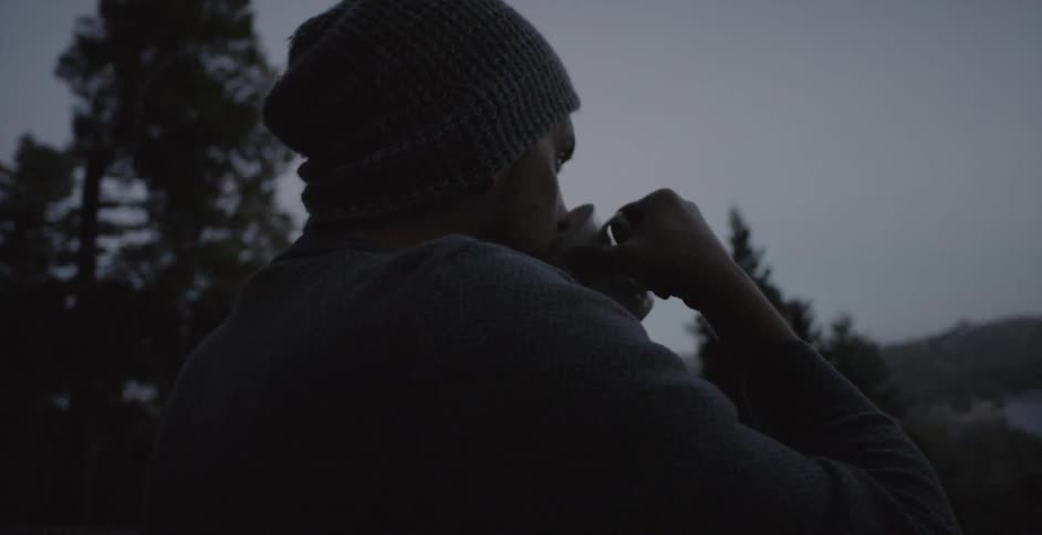 Man taking a sip of his drink while outdoors on a cool day surrounded by trees