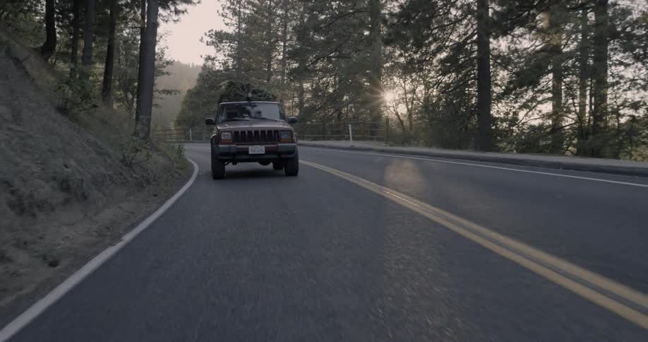 An suv with a christmas tree on the roof travels on a mountain road
