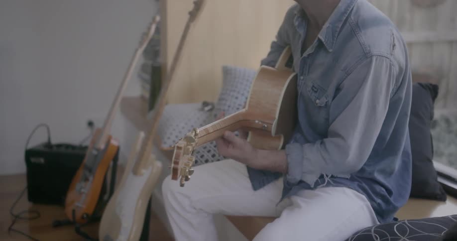 A man plays guitar and sings while sitting on a window seat