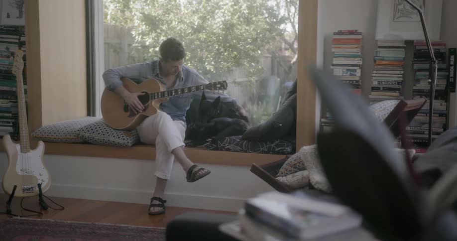 A man plays guitar while sitting on a bench window