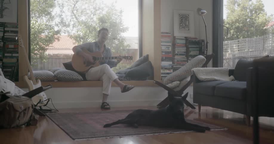 A man plays guitar while sitting on a bench window