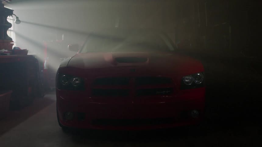 A red muscle car is parked in a garage